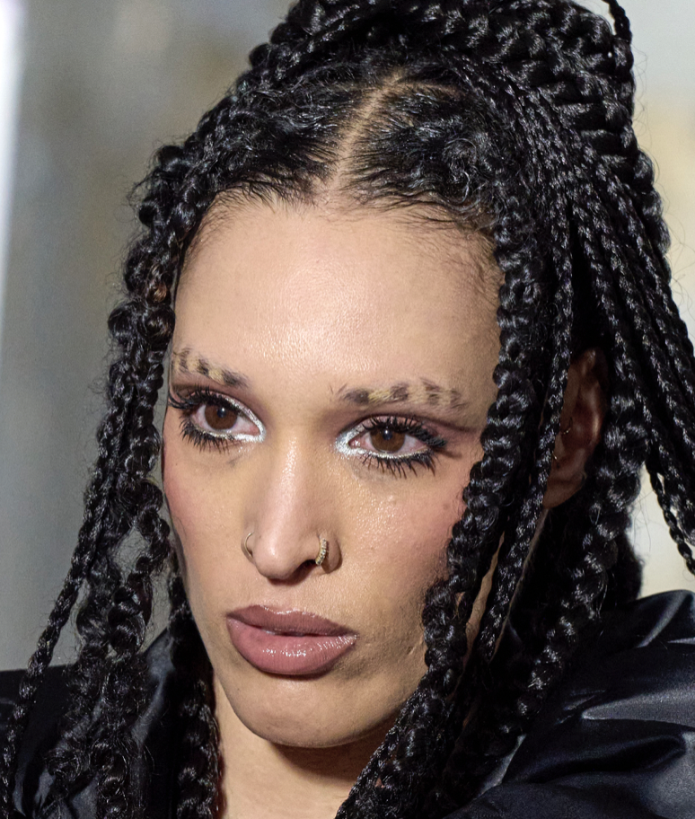 A person with black braids and piercingsDescription automatically generated