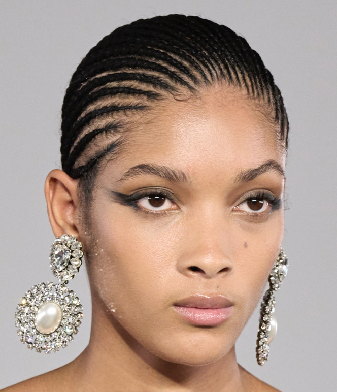 A person with braided hair and large earringsDescription automatically generated