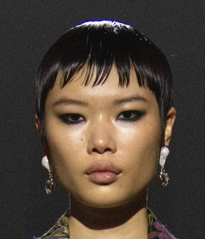 A person with short black hair and earringsDescription automatically generated