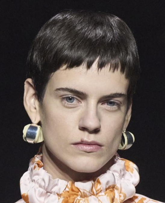 A person with short hair wearing earringsDescription automatically generated