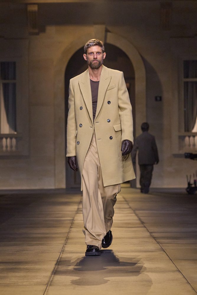 A person in a long coat walking down a runway Description automatically generated