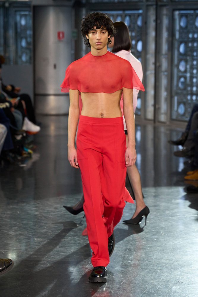 A person in a red shirt and pants walking down a runway Description automatically generated