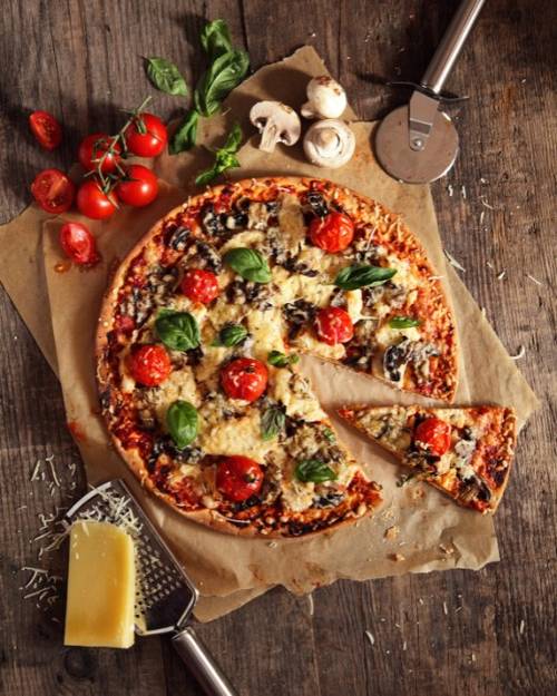 A pizza with tomatoes and basil on a wooden surface Description automatically generated